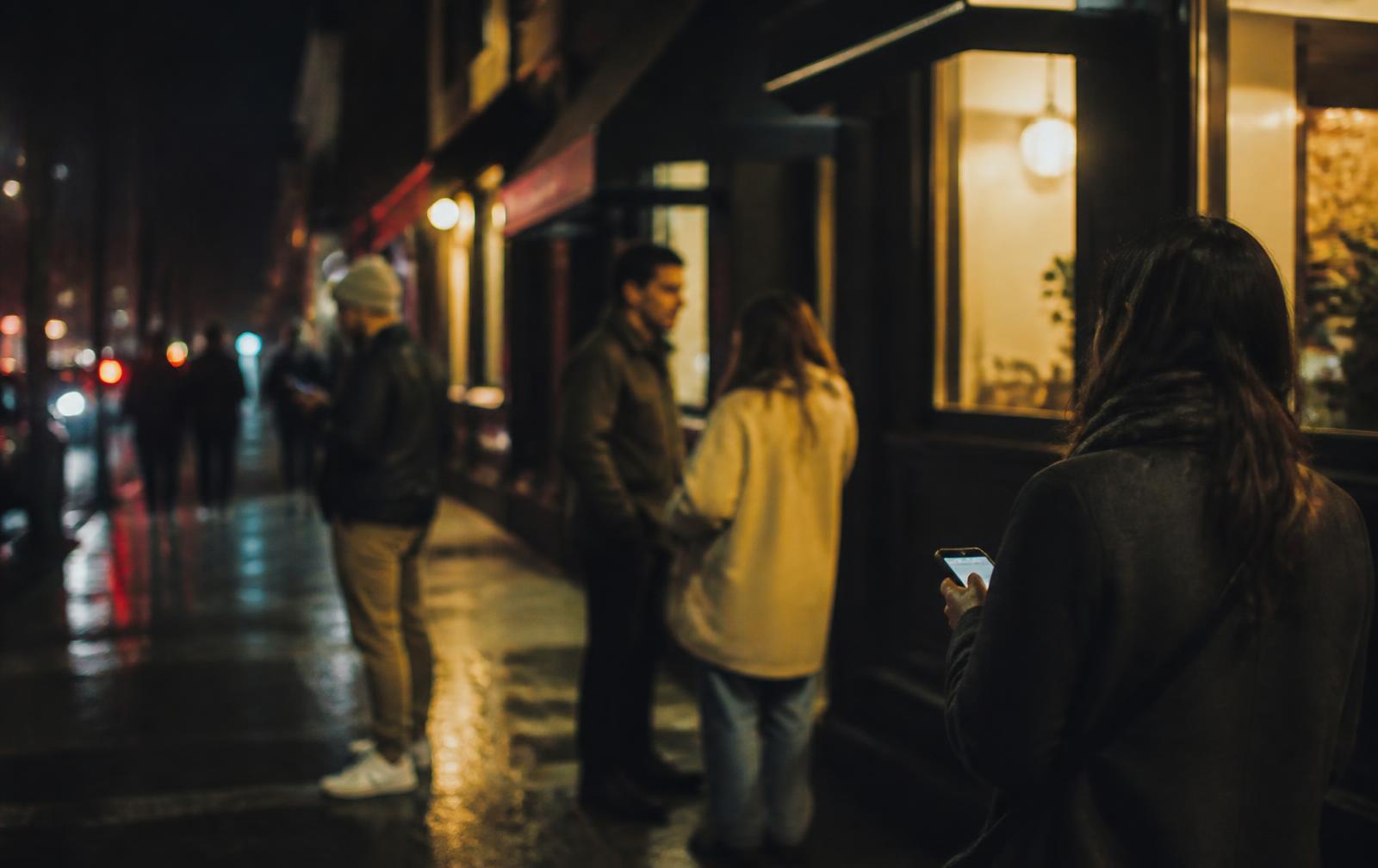 People talking on a rain-slicked New York sidewalk at night